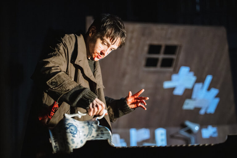 Connor Curren as Raskolnikov pouring water from a jug. He has blood on his face.