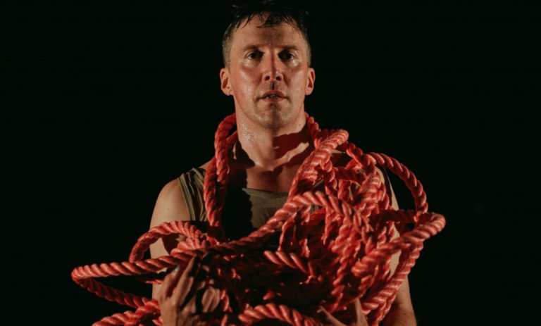 a man wrapped in red rope stands in front of a black background