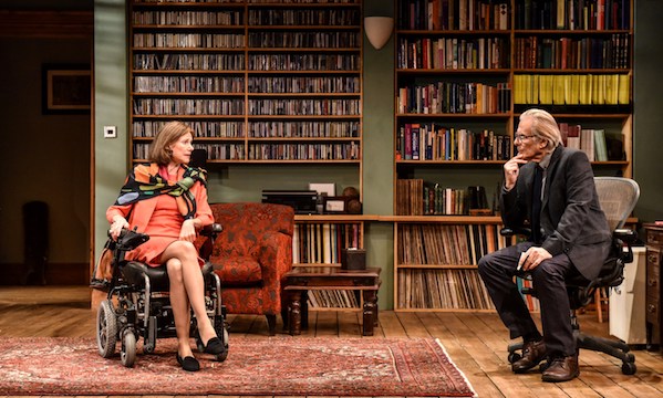 A lady in a wheelchair and a man face each other in a book-filled office