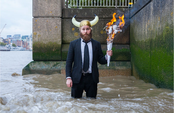 man in viking helmet standing in river with torch
